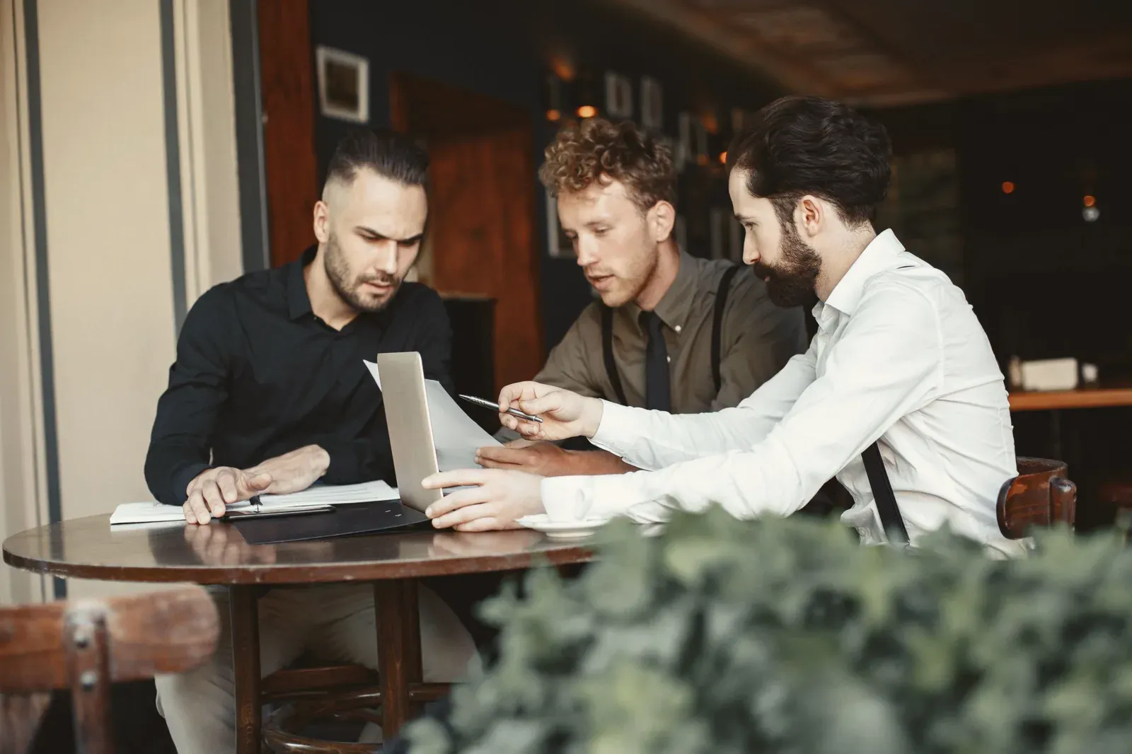 Drie mannen kijken samen naar een laptop aan een tafel in een café