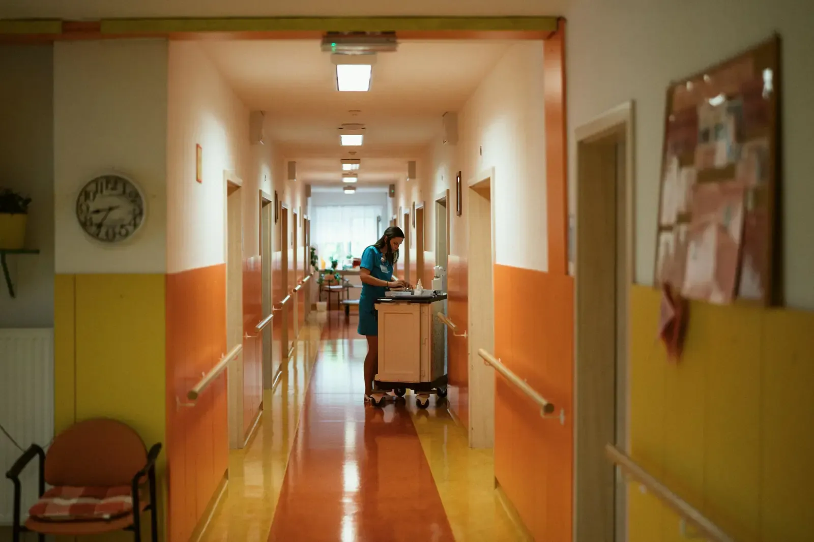Een medewerker met een schoonmaakkar in de gang van een zorginstelling